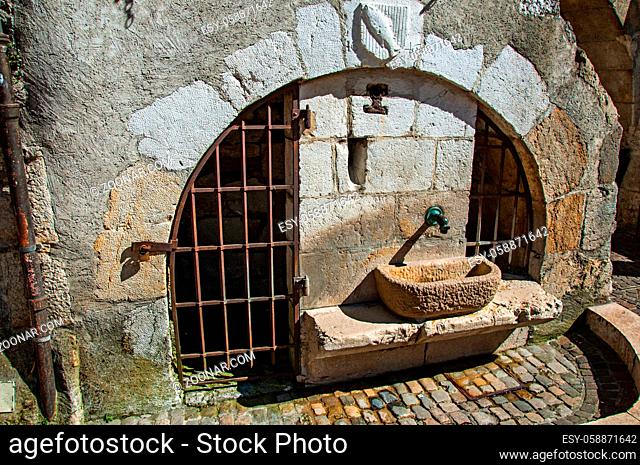 Old stone water fountain with iron gates and heraldic shield on the arch, historical city center of Annecy. Located in the department of Haute-Savoie