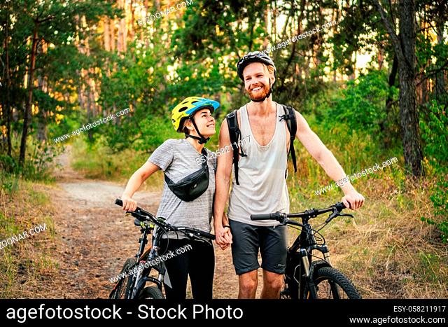 Cheerful couple pushing bicycles and walking along the forest road. Happy couple with bicycle walking through park and talking and laugh