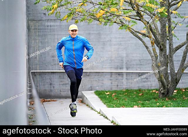 Smiling mature man running with dedication on footpath