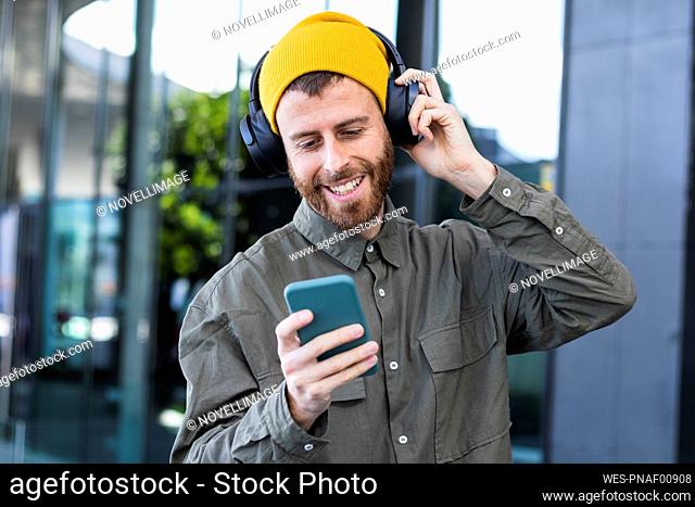 Man listening music on headphones through mobile phone near building