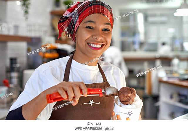 Young woman working in ice cream parlour, filling cup with icecream