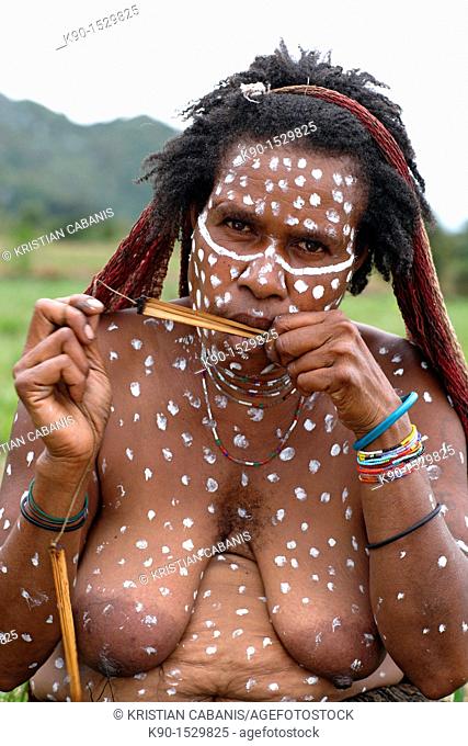 Half body image of local Papuan woman, looking at the camera with traditional face painting, playing a traditional instrument, Baliem Valley festival