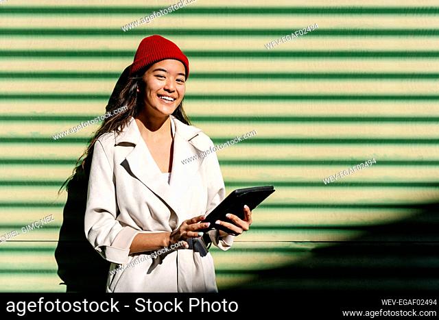 Smiling young woman with tablet PC in front of wall