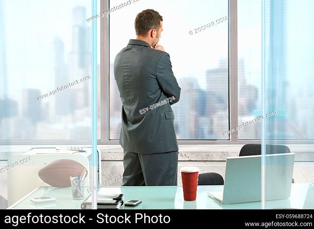 Businessman thinking in office, looking out of windows to downtown vista