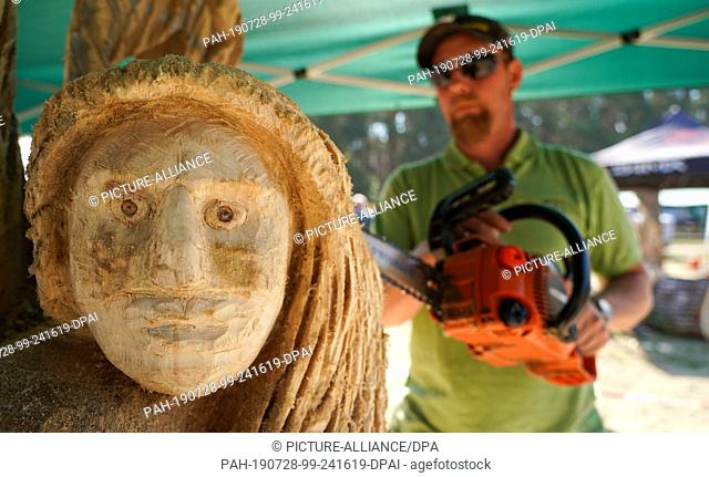 28 July 2019, Saxony-Anhalt, Tornau: The wood artist Dan Nissen from Denmark works with a chainsaw on his sculpture ""Fee"" on the wood sculpture meadow in...
