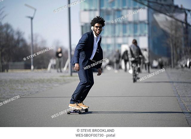 Smiling businessman riding longboard in front of skyscraper