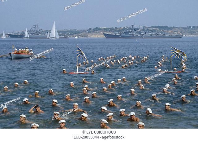 Navy Day. Sailors swimming in the sea in formation with battleships behind