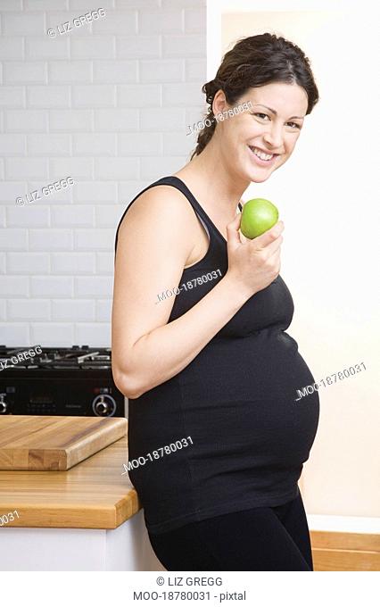 Pregnant woman eating apple in kitchen portrait