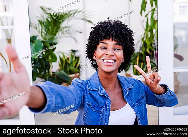 Happy woman showing peace sign gesture and taking selfie in doorway