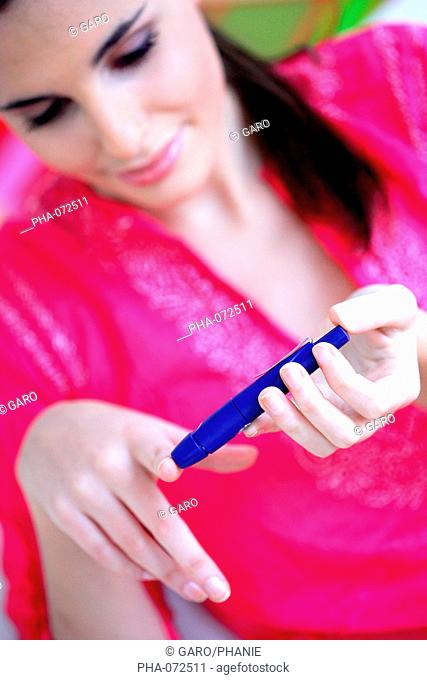 A diabetic person is checking her blood sugar level self glycemia. A drop of blood obtained with a pen-like lancing device is placed on a test stick and...
