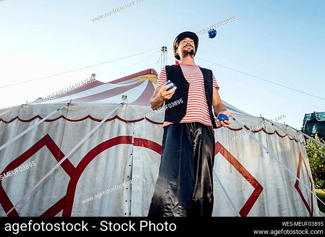 Male artist juggling balls while standing in front of circus tent
