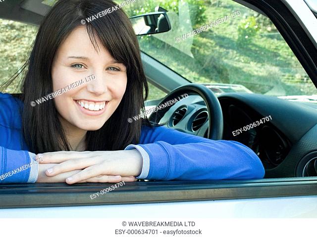 Happy teen girl smiling at the camera sitting in her car outdoor