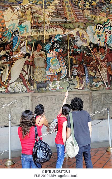 Group of visitors looking at mural by Diego Rivera depicting life before the Conquest in the Palacio Nacional