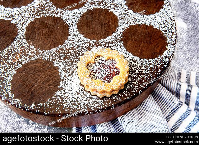 Close-up of one Linzer cookie dusted with powdered sugar on round wood board