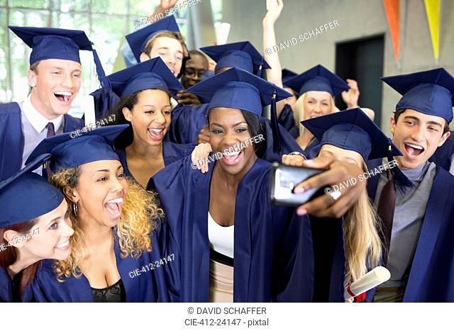 Group of smiling students in graduation gowns taking selfie on graduation day