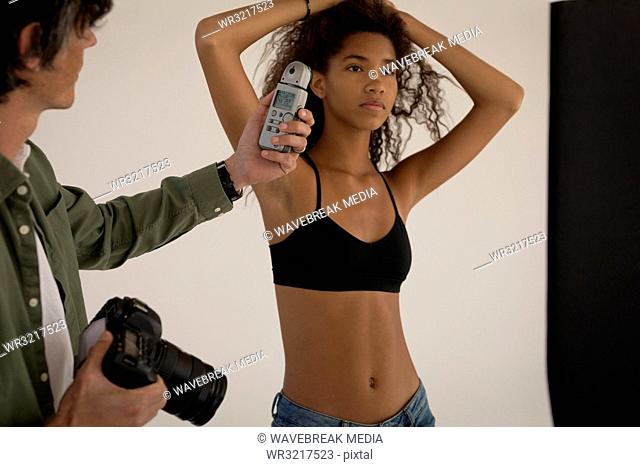 Photographer measuring light with light meter on female model