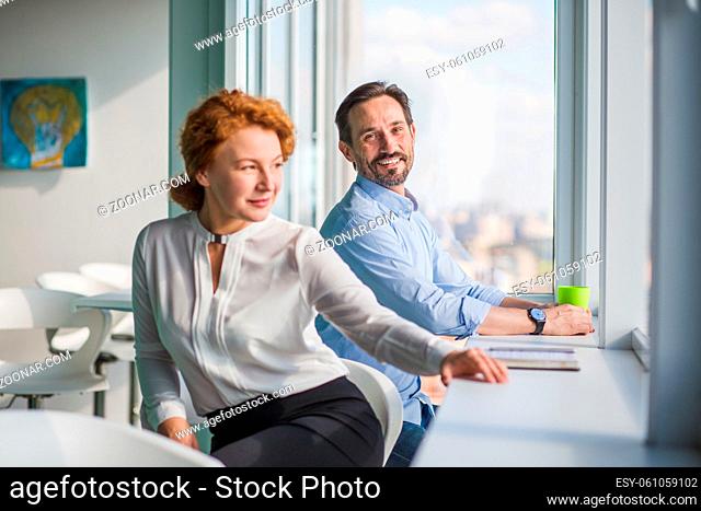 Businessman and businesswoman having rest during work. Handsome man looking at his colleague in office interior. Office break concept