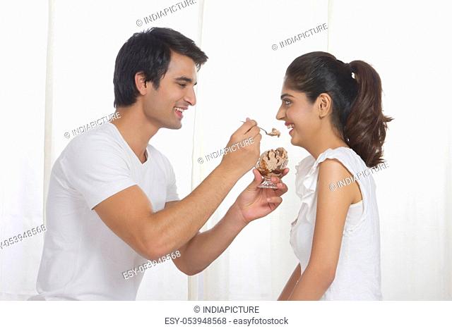 Side view of loving man feeding woman chocolate ice-cream at home