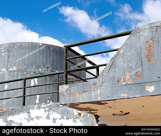 an old crumbling concrete military bunker type structure with rounded windowless surfaces and a green railing against a blue cloudy sky