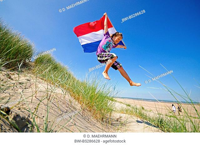 energetic boy jumping out of the dunes with a dutch flag, Netherlands