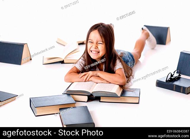 cute funny little child girl in denim is reading book on the floor with group of books around her on white background. Children and education