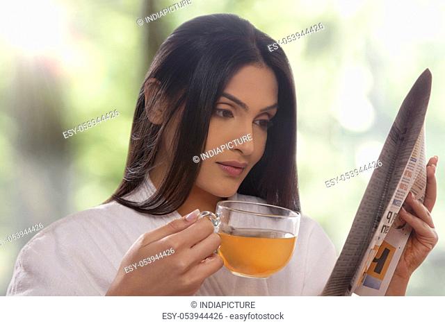 Young woman reading newspaper while drinking tea