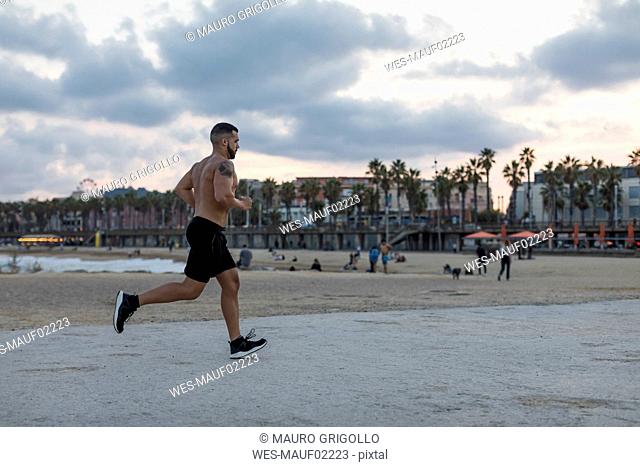 Barechested muscular man running on waterfront promenade