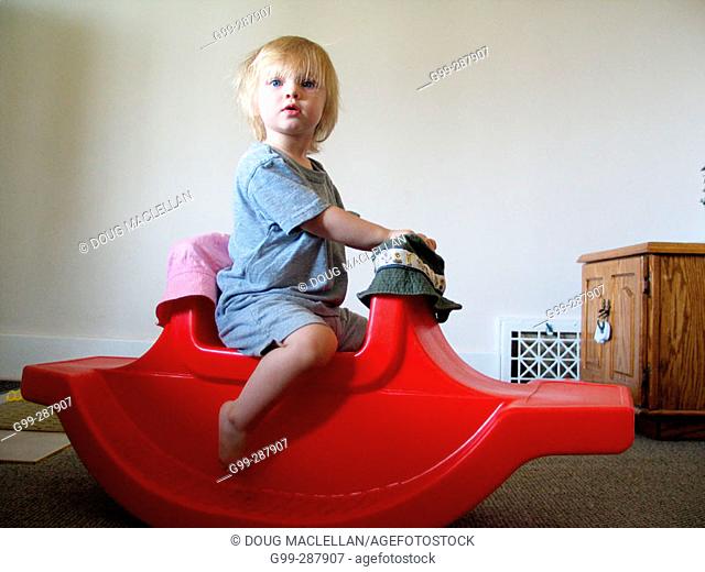 18 month old toddler playing on red rocking horse in her home
