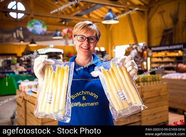21 April 2020, Brandenburg, Klaistow: Saleswoman Iwona shows two packets of pre-cooked fresh asparagus in the farm shop. The pre-cooked food has been available...