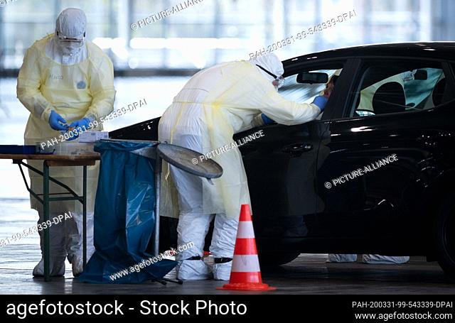 31 March 2020, Lower Saxony, Hanover: Doctors take a smear test from patients in the newly established Corona Drive-In test centre at the Hanover exhibition...