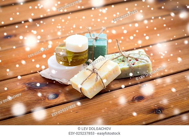beauty, spa, bodycare, bath and natural cosmetics concept - handmade soap bars on wooden table over snow