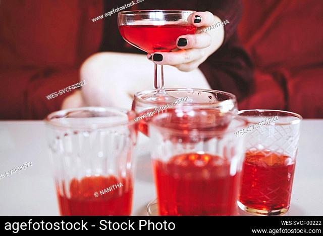 Hand of woman holding champagne coupe with red alcoholic drink