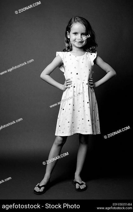 Studio shot of cute young girl with blond hair wearing white dress against gray background in black and white