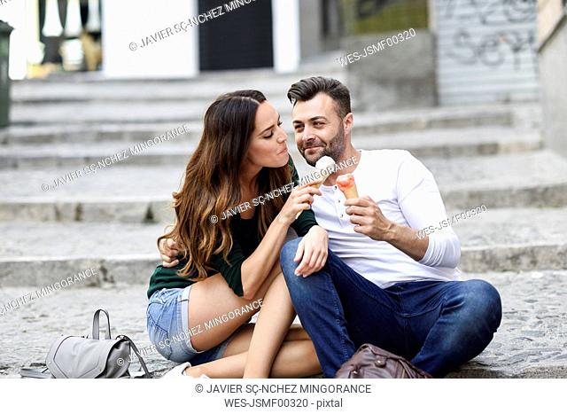 Tourist couple sharing ice cream cones in the city