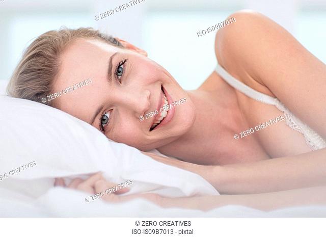Portrait of young woman lying in bed, smiling