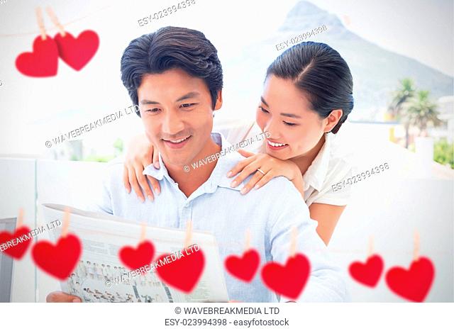 Hearts hanging on a line against couple reading a newspaper together