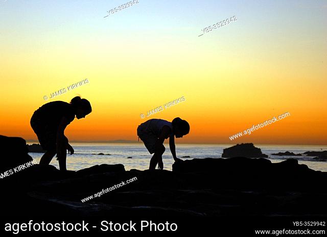 Two young girls enjoy walking along a tide pool at sunset