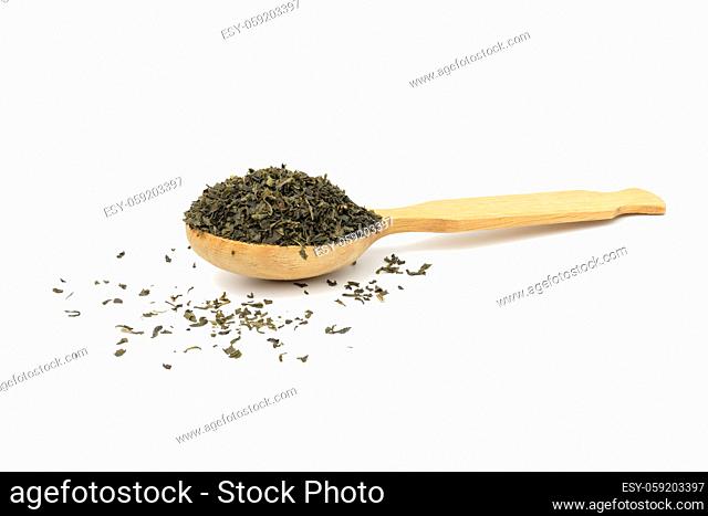dried crushed green tea leaves in a wooden spoon on a white background