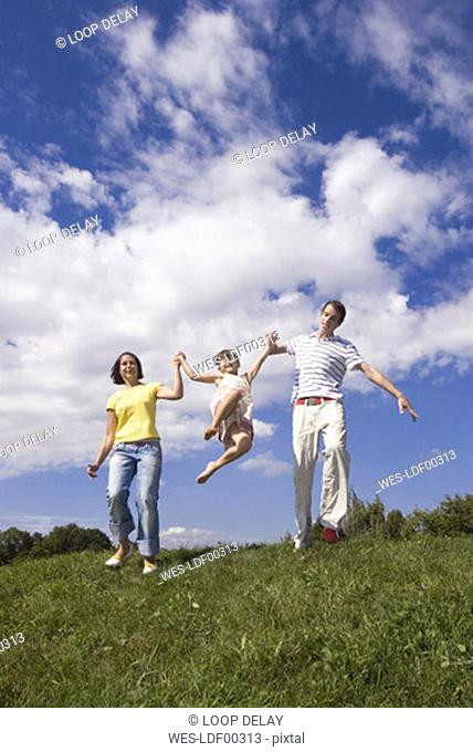 Parents lifting daughter (7-9) in meadow, low angle view