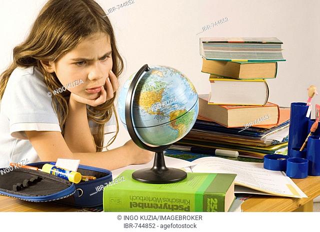Nine-year-old girl doing homework at her desk, looking at a globe
