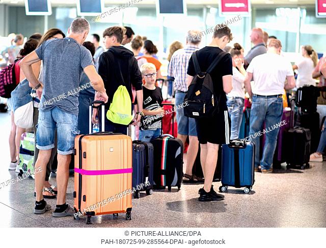 25 July 2018, Langenhagen, Germany: Passengers are standing with their luggage in front of a check-in counter in the departure hall of Hanover Airport