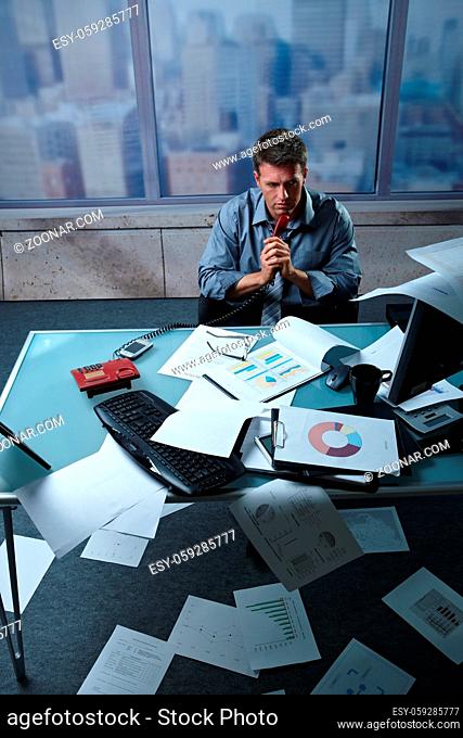 Tired businessman calling from office papers lying all around, picture taken from high angle