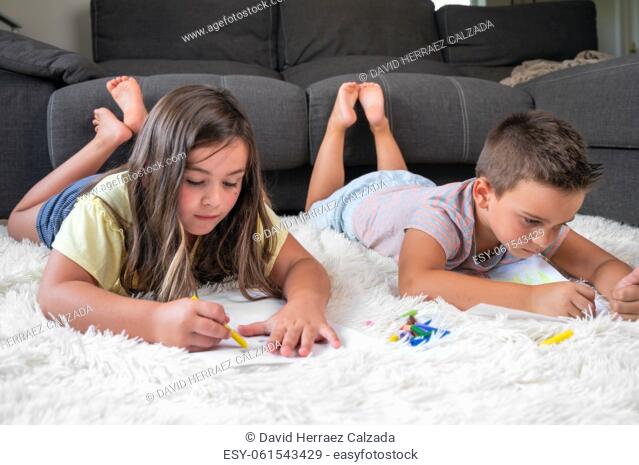 Siblings playing together at home. little boy and girl lying on the carpet and drawing on white sheets of paper with colorful crayons