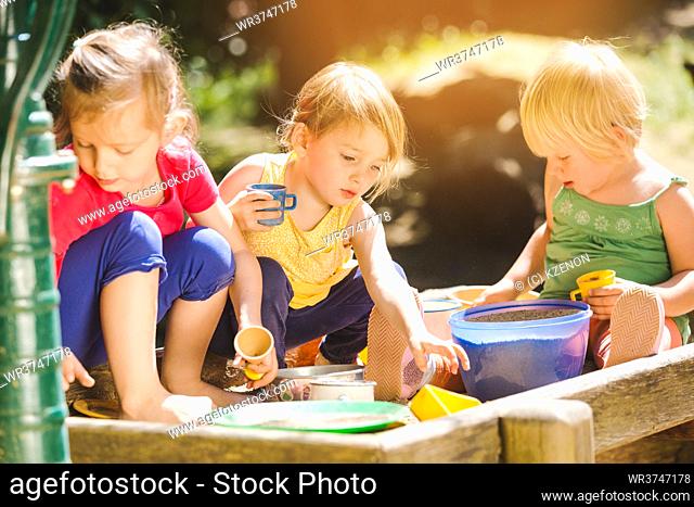 Group of girl children playing in the sandbox with all their toys