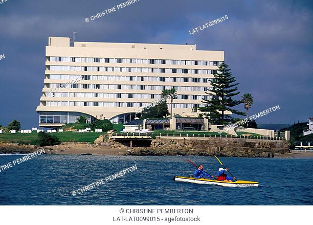 Beacon Islands Hotel. Large white modern building. Beach. Two people in canoe