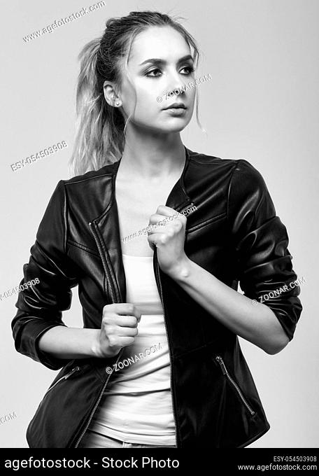Monochrome portrait of young female with black leather jacket. Young pretty woman on gray background
