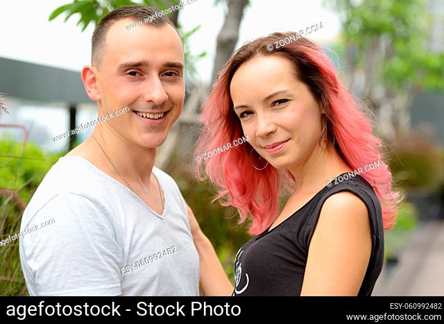 Portrait of handsome man and beautiful woman with pink hair as couple together and in love in the park outdoors