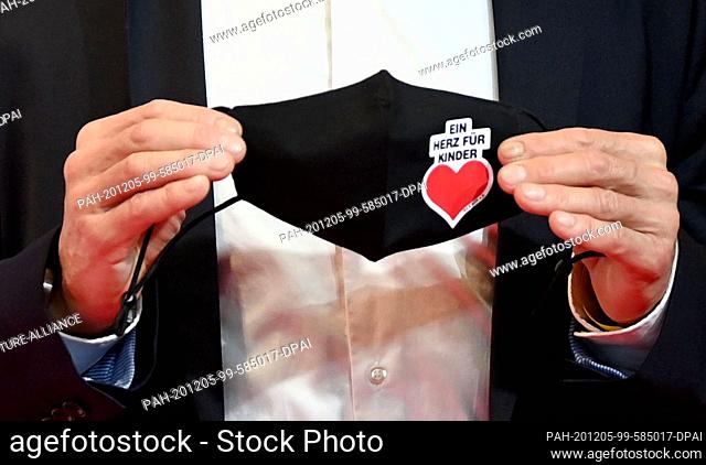 05 December 2020, Berlin: Actor Hannes Jaenicke holds a mouth-and-nose protector with the logo of ""Ein Herz für Kinder"" when arriving at the TV fundraising...