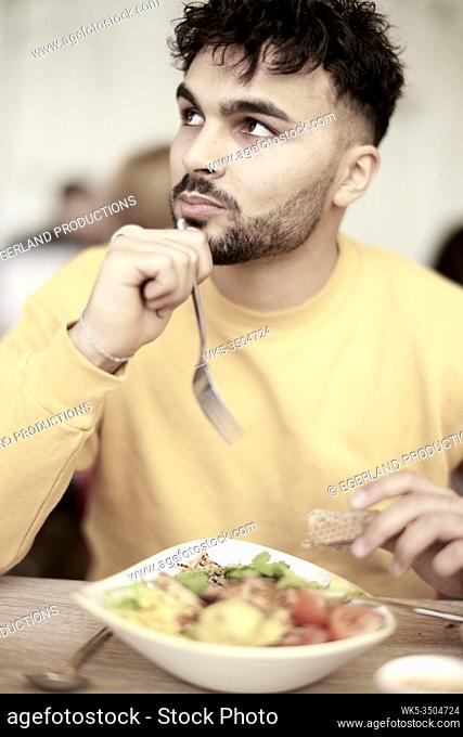 Young man sitting at table in restaurant, eating salad
