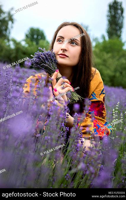 Thoughtful woman with bouquet of fresh lavender flowers at field